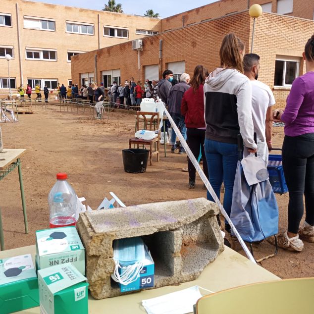 Persones fent cua a l'institut per recollir aliments i material Persones fent cua a l'institut per recollir aliments i material